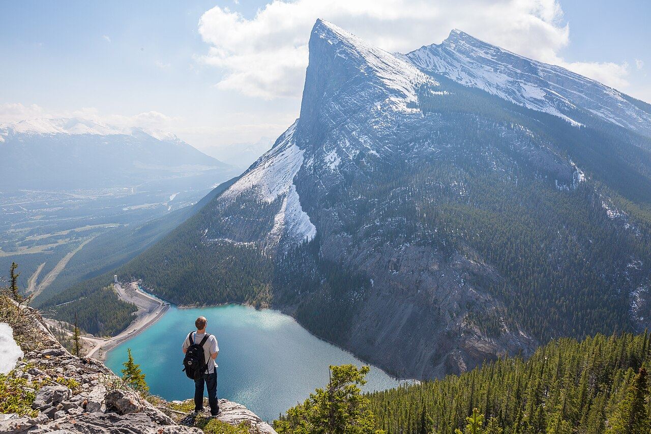 A backpacker on a high ledge above a turquoise mountain lake