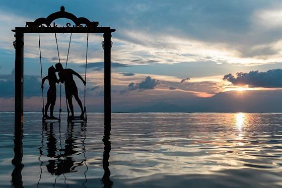 A couple on a swing over the sea at sunset