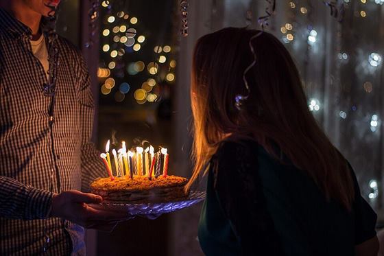 A birthday cake with lit candles carried to a guest