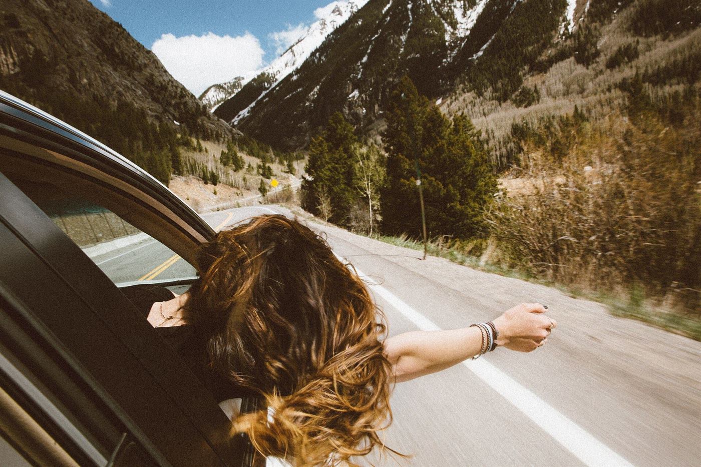 A passenger with her arm out of the car window on a mountain road