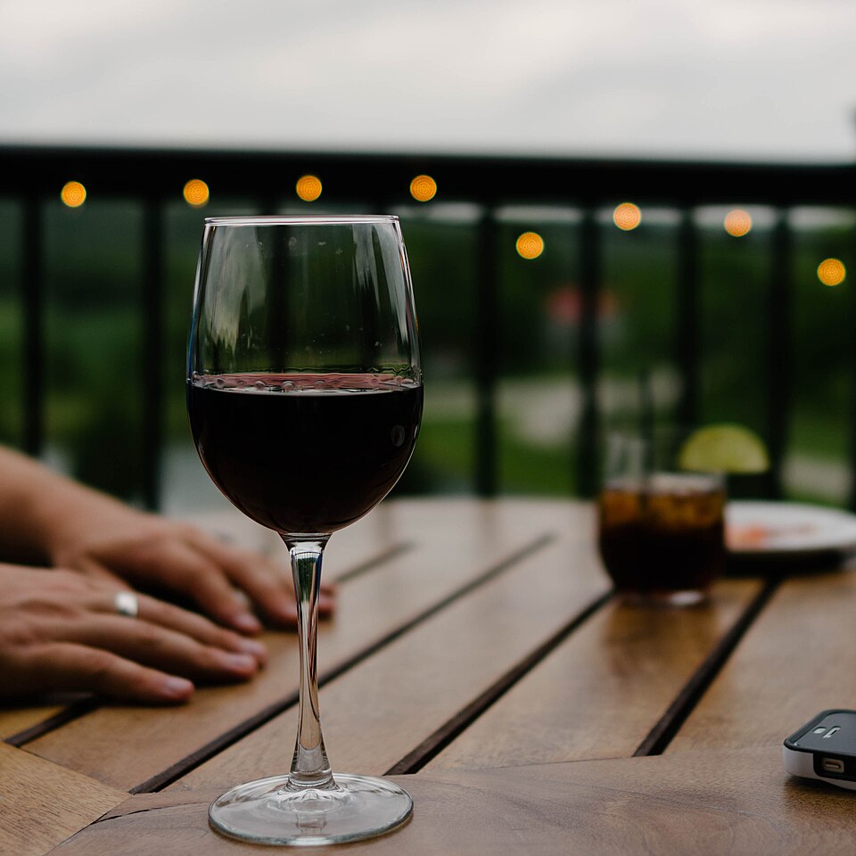 A glass of red wine on a dinner table under string lights