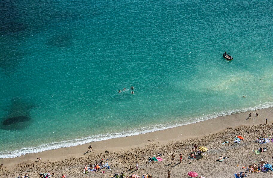 Holidaymakers on a sandy beach beside turquoise water