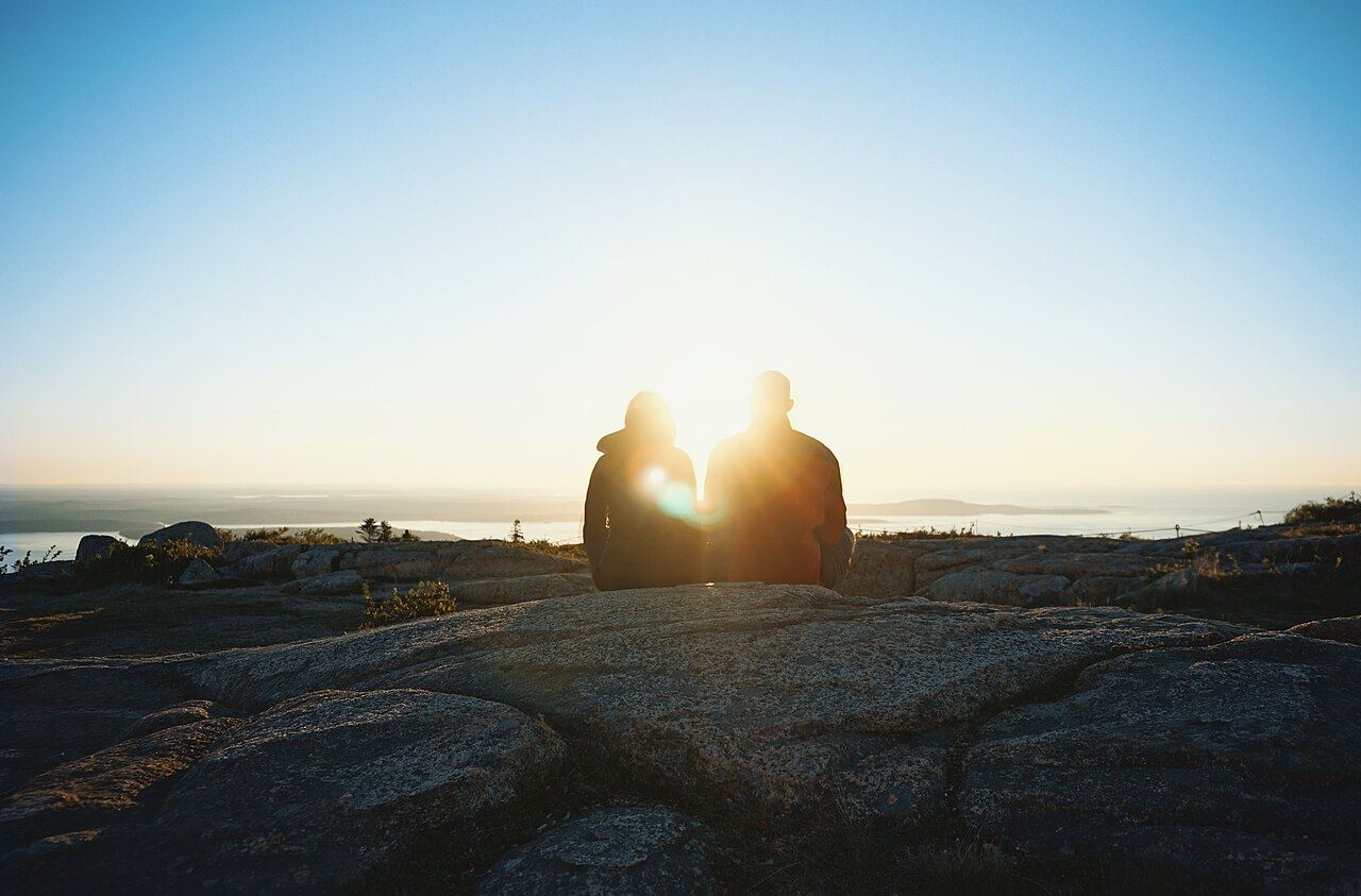 A couple sitting together on a hilltop, watching the sun set