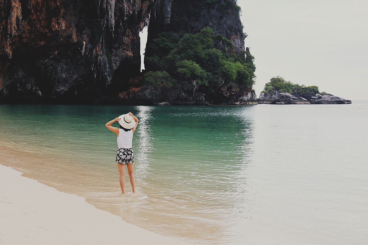 A traveller wading in clear water below limestone cliffs in Krabi