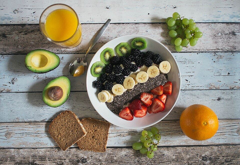 A bowl of fruit with avocado, bread and orange juice