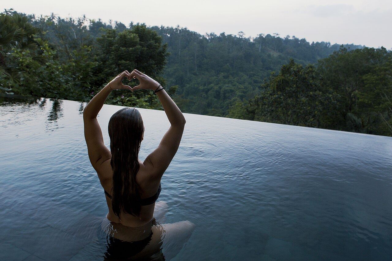 A woman meditating in an infinity pool above a forested valley